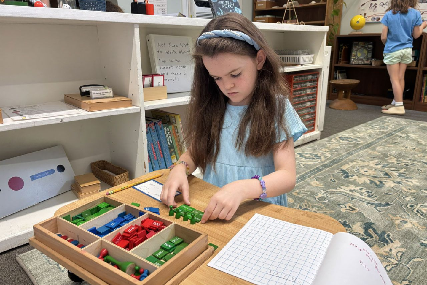 Montessori child calculating a problem using the Stamp Game material