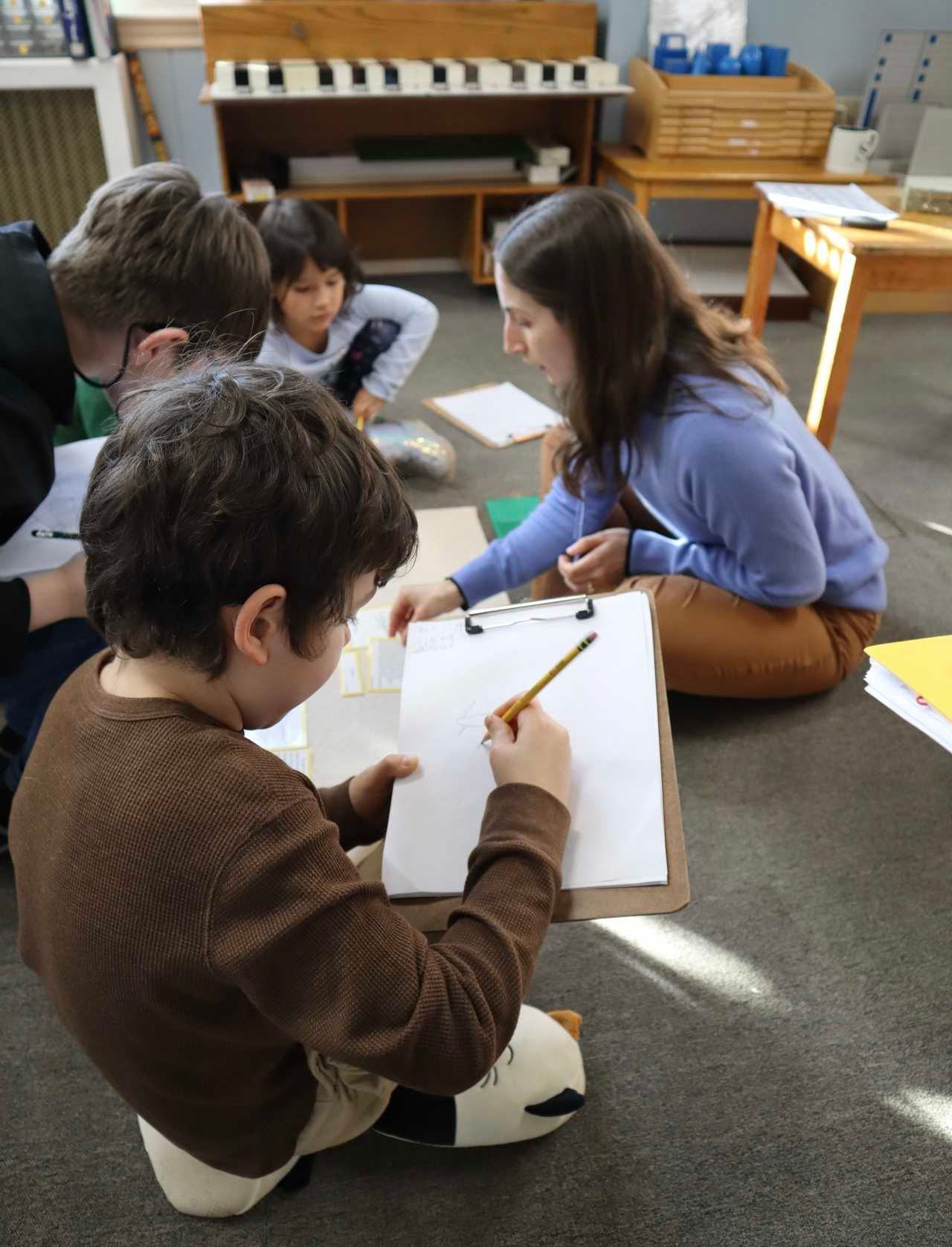 Elementary students using Montessori math materials and the Stamp Game for hands-on learning with their teacher in a classroom setting