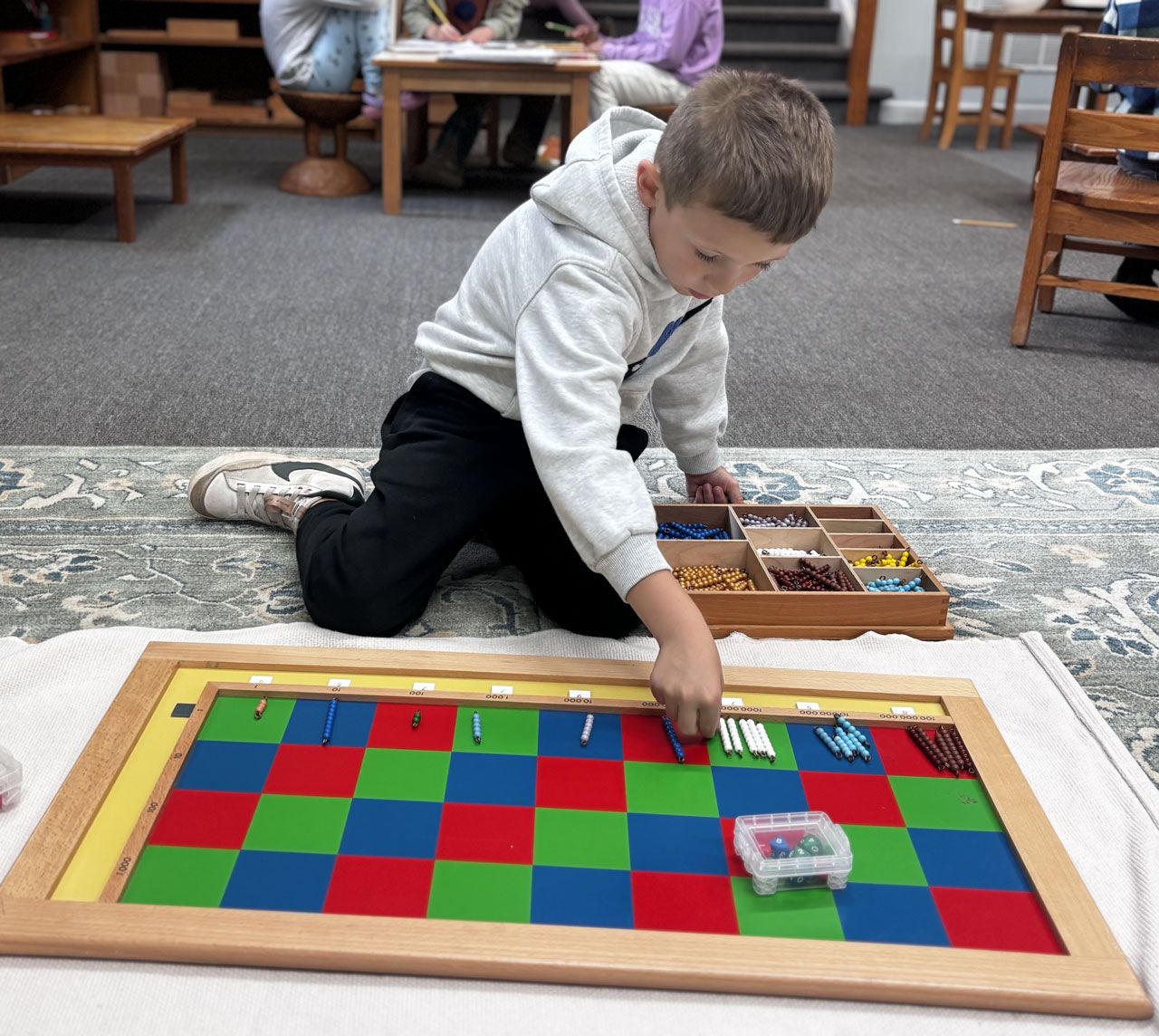 Montessori elementary student using a colorful checkerboard and bead bars to solve a long multiplication math problem