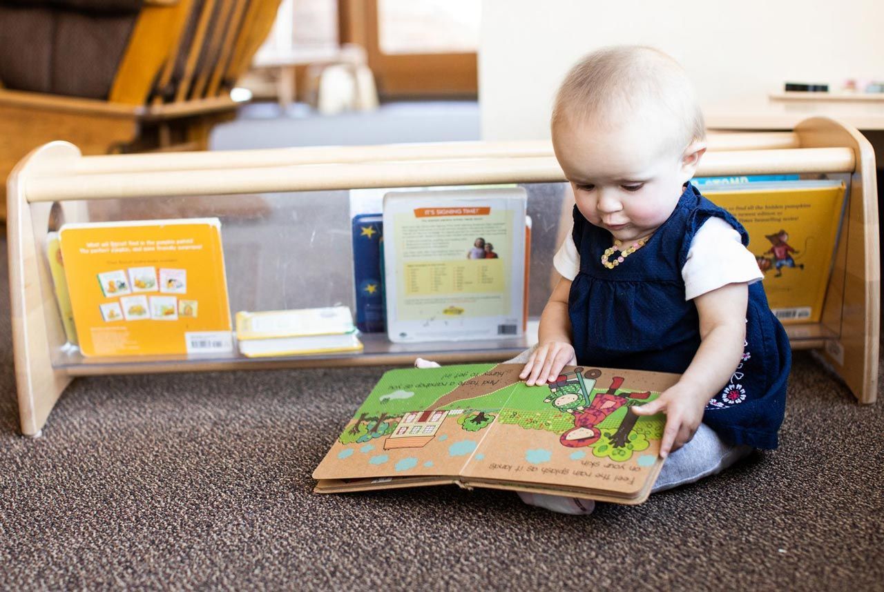 A Montessori infant is sitting on the floor and looking at a book.
