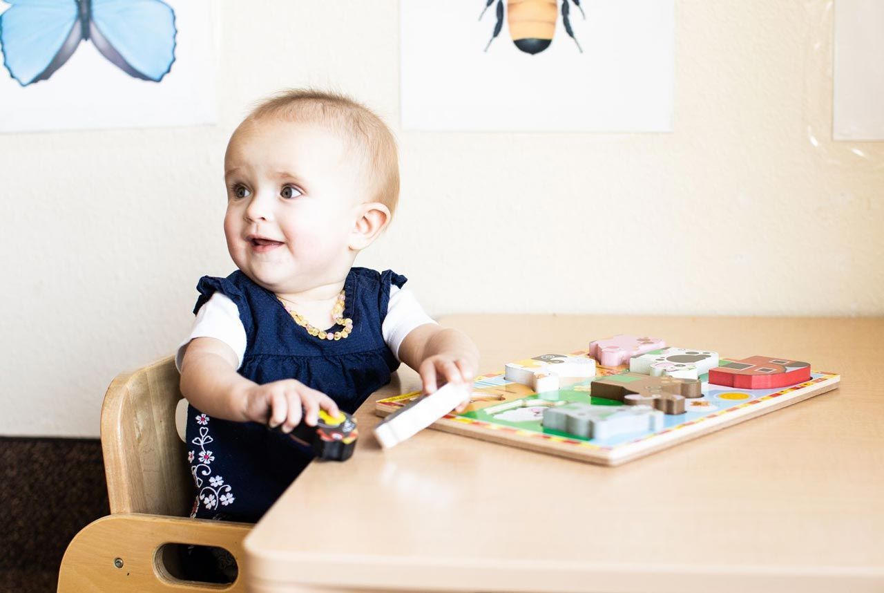 A Montessori infant is sitting at a table with a puzzle.