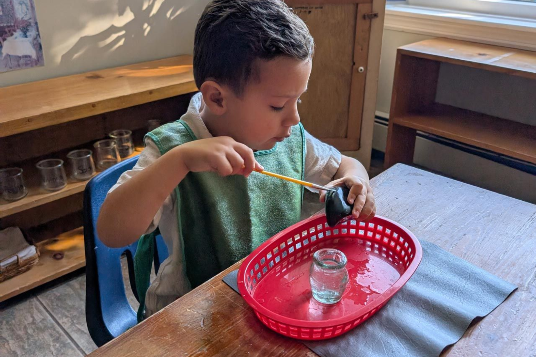 Montessori primary child focused on painting a rock at a wooden table