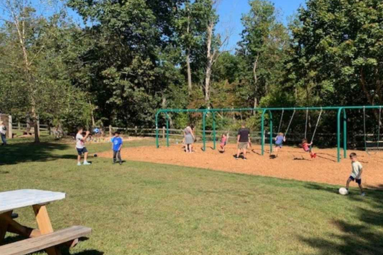 Students enjoying outdoor recess and gross motor activities at a Montessori school playground with swings and open green space