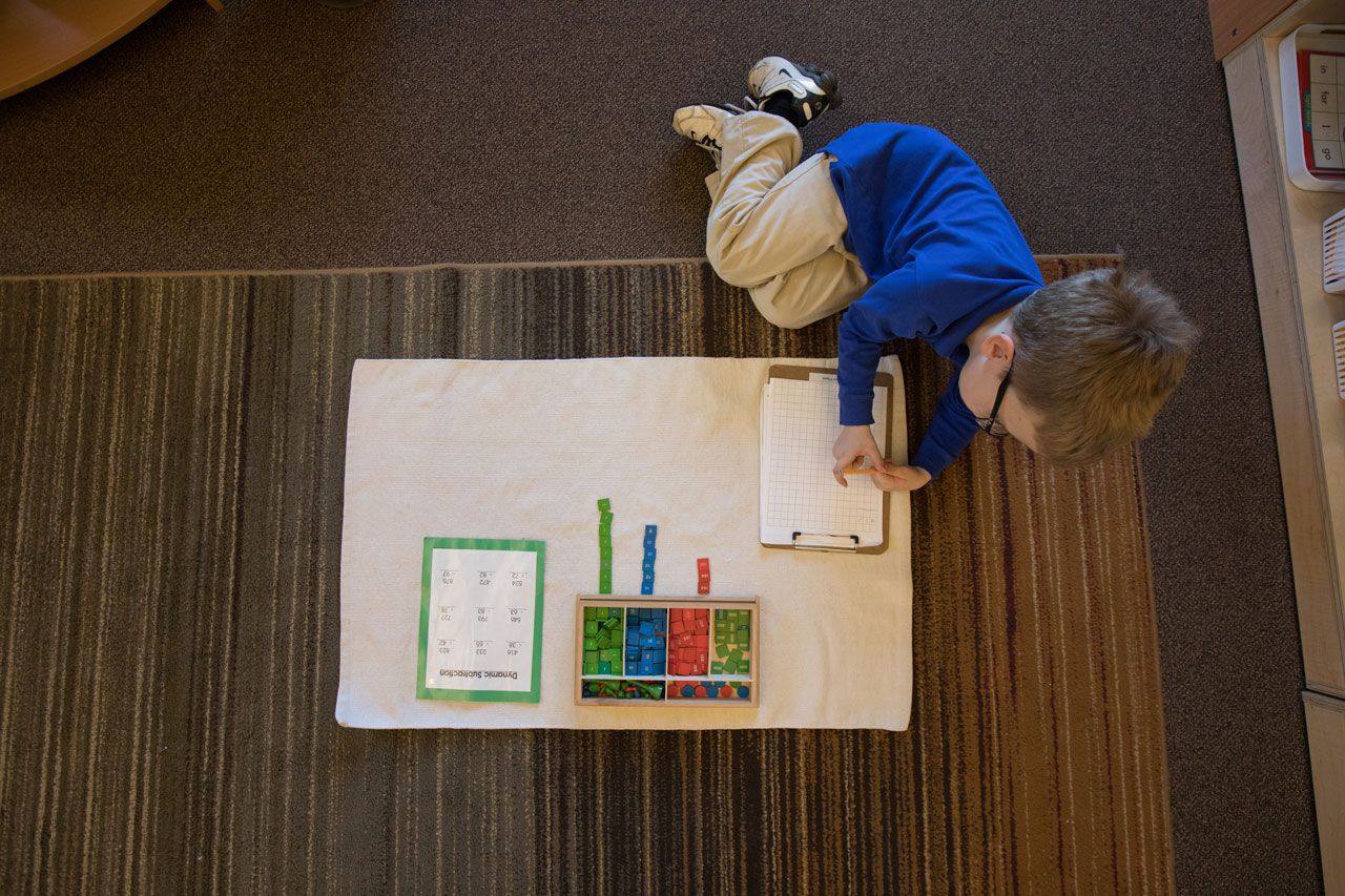 Overhead view of a Montessori student working on a dynamic subtraction lesson using the stamp game on a floor mat