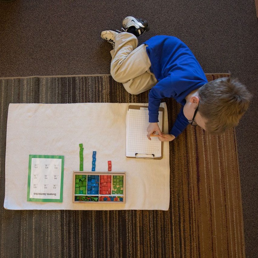Montessori student working on a dynamic subtraction lesson using the stamp game on a floor mat
