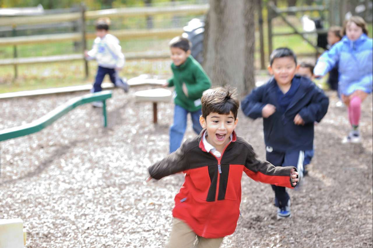 Primary students engaging in active gross motor play and running exercises at a Montessori school outdoor playground