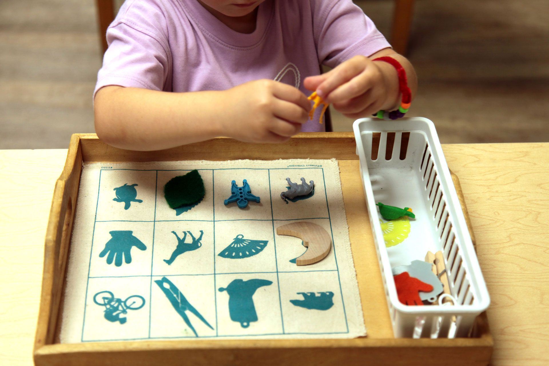Montessori toddler matching small three-dimensional objects to corresponding pictures on a lesson mat