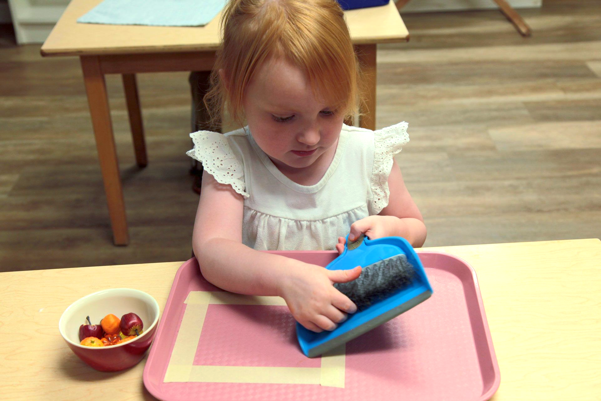 Montessori toddler learning a practical life skill, sweeping on a tray with a small dustpan and brush
