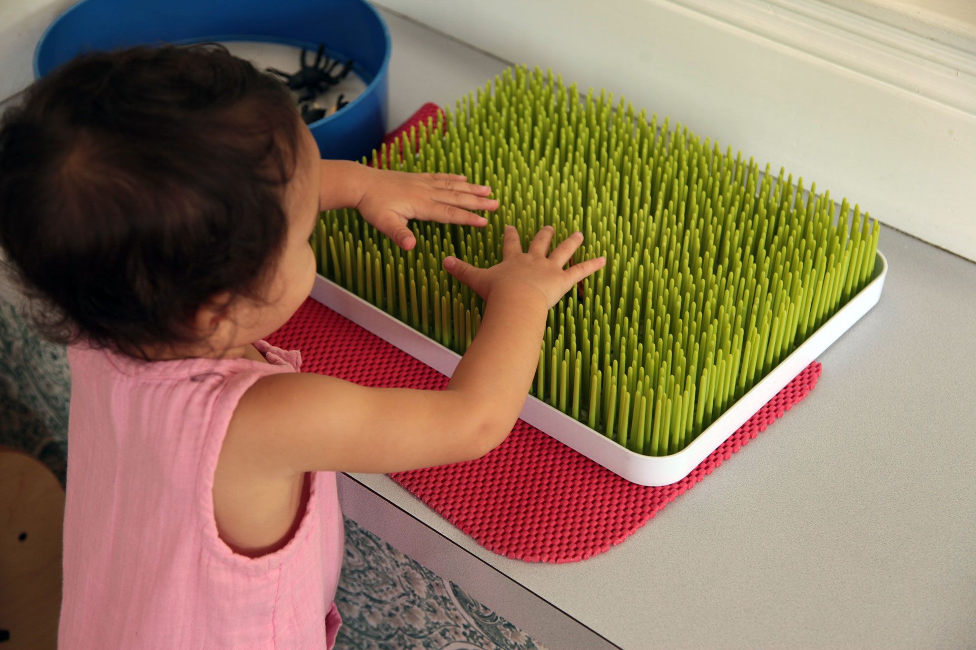 Montessori toddler reaching out to touch a green spikey sensory mat on a table
