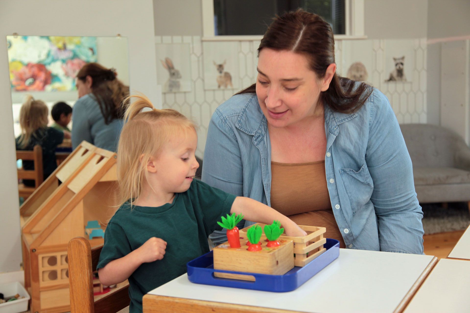 Montessori teacher assisting a toddler with a wooden carrot harvesting practical life material