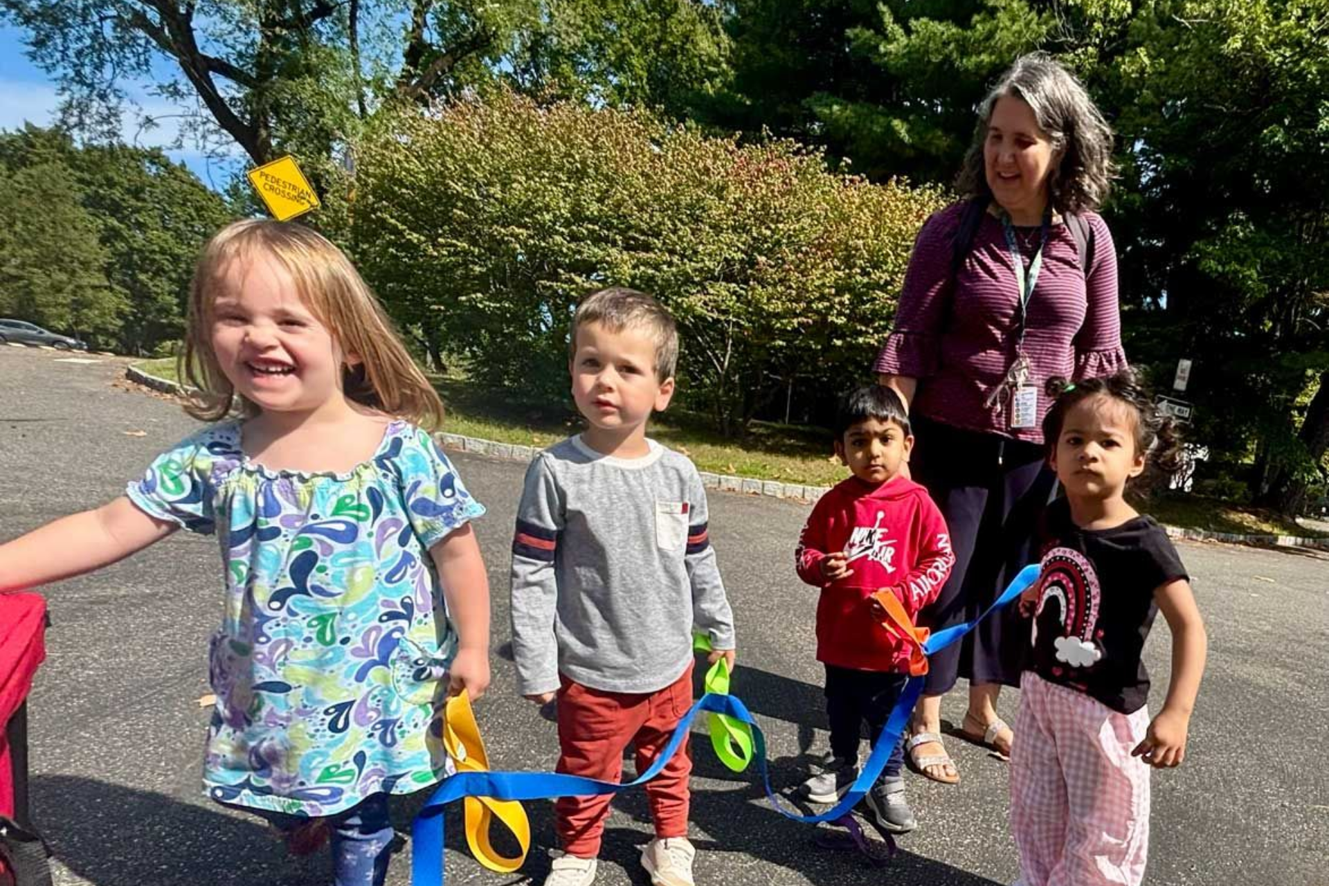 Montessori toddlers and a teacher playing with colorful ribbons on the playground