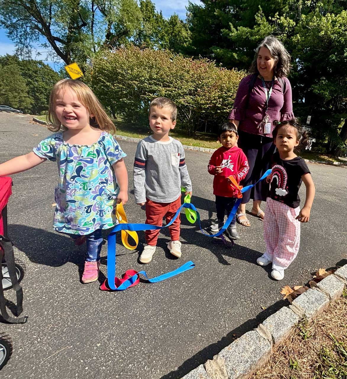 Montessori toddlers and a teacher playing with colorful ribbons on the playground
