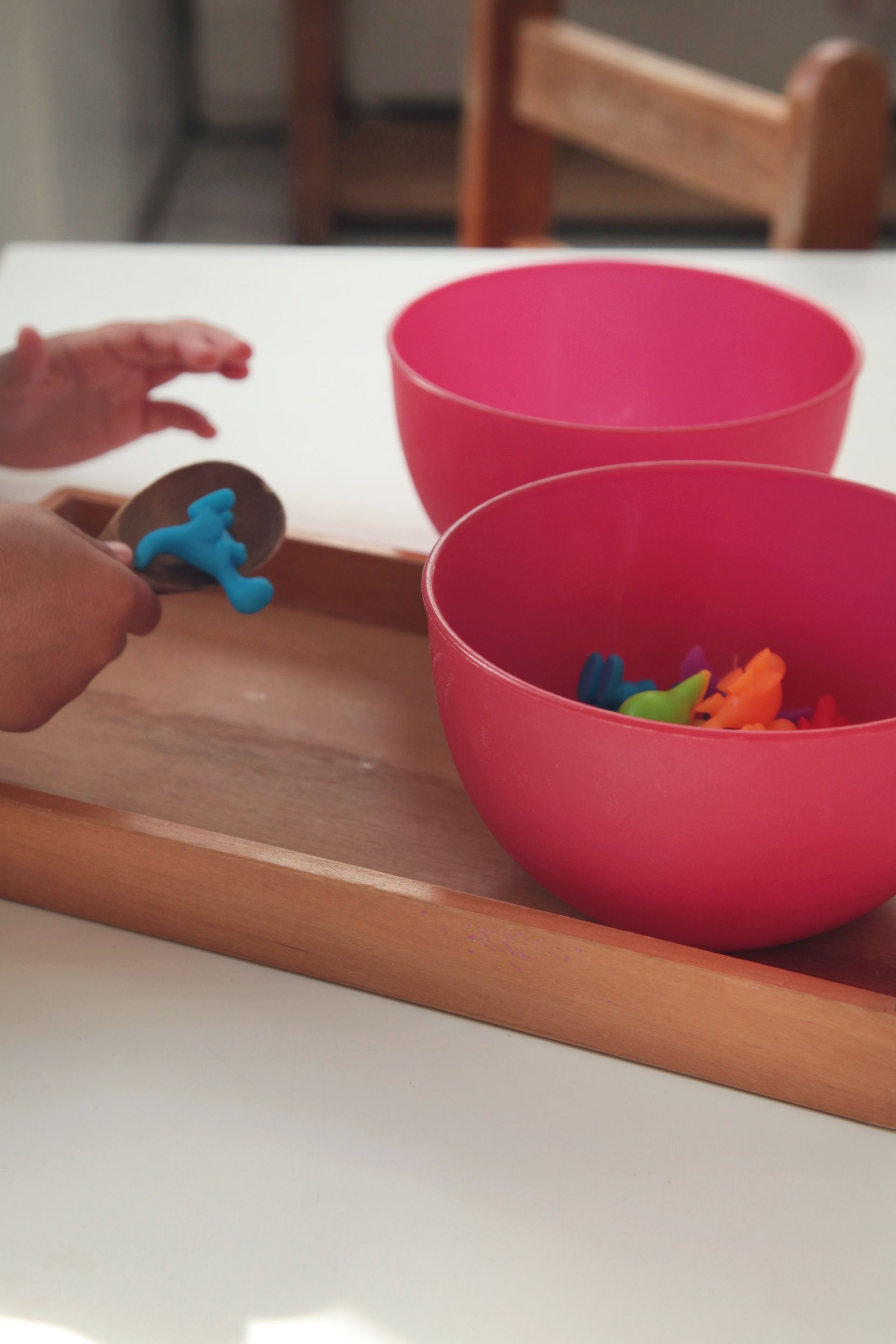 Child’s hands placing a blue toy near two pink bowls on a wooden table