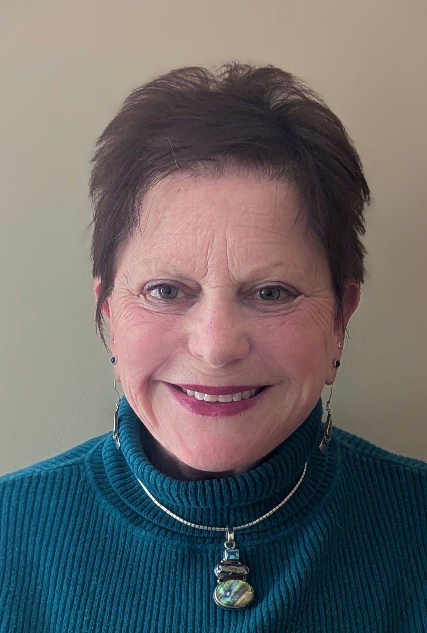 Two people holding hands, one wearing a gray sweater, the other wearing a patterned blazer, indoors.