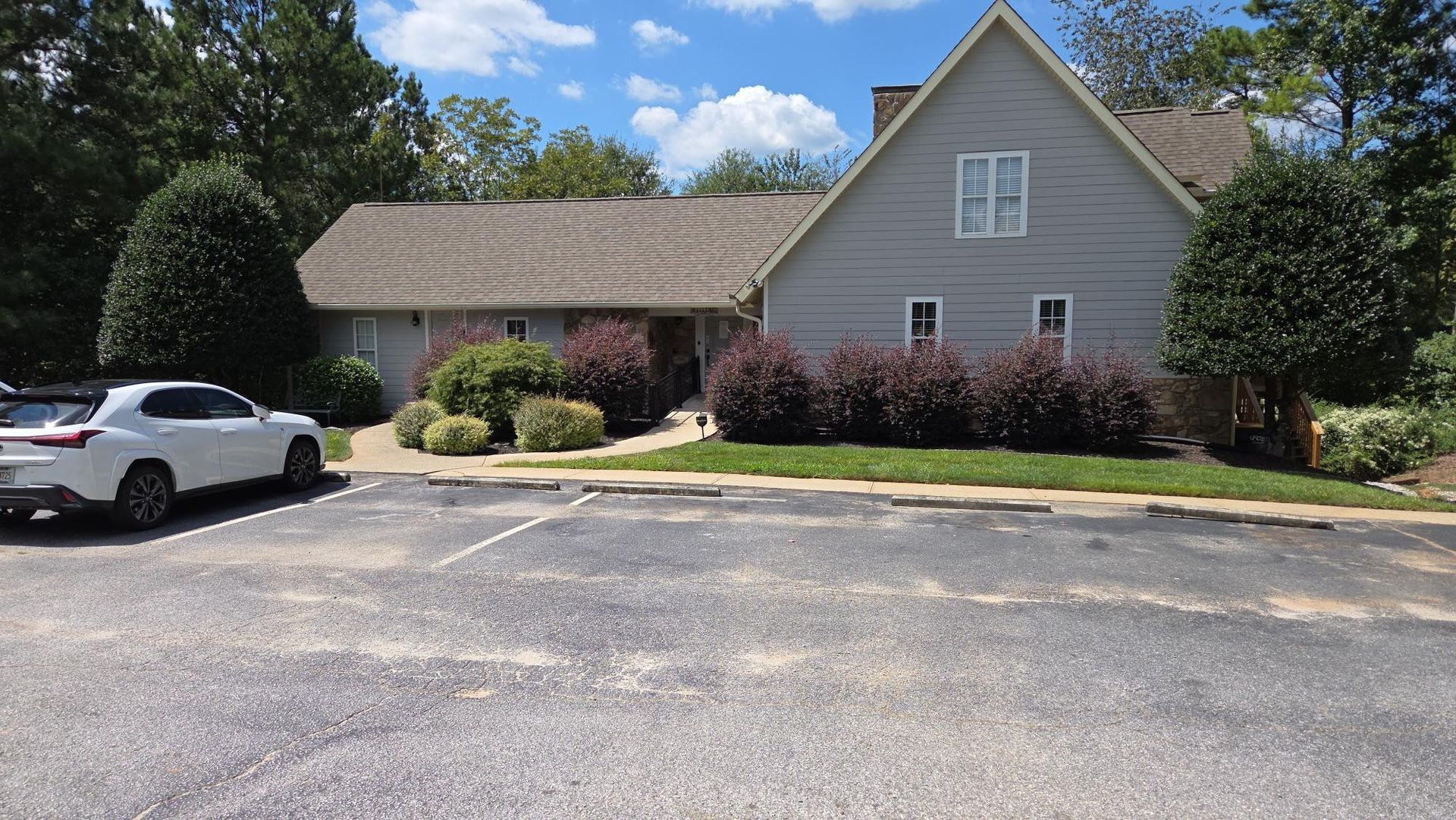 Person in hard hat and orange vest inspects a two-story house, holding a tablet.