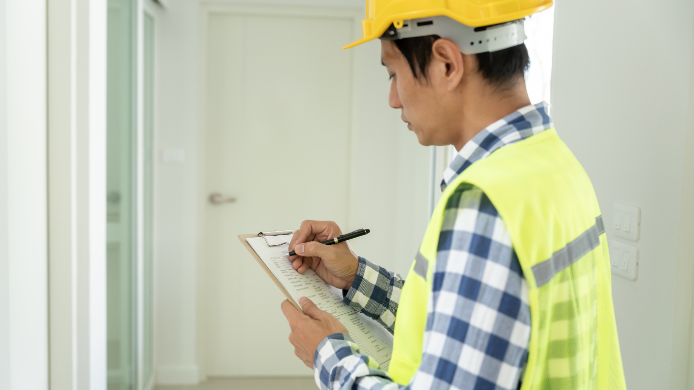 Construction worker in yellow helmet and vest, writing on a clipboard in a white interior.