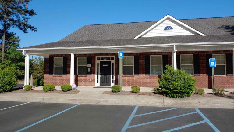 Brick building with a porch, black shutters, and accessible parking signs.