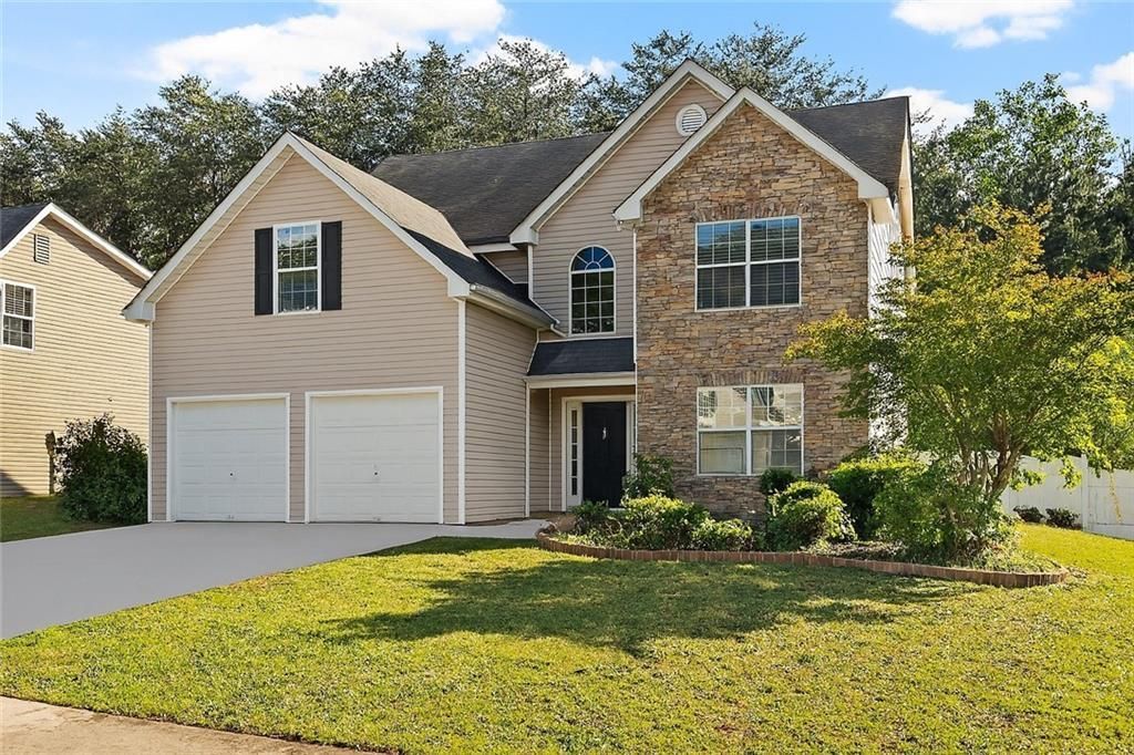 Two-story house with beige siding, stone facade, two-car garage, and green lawn.