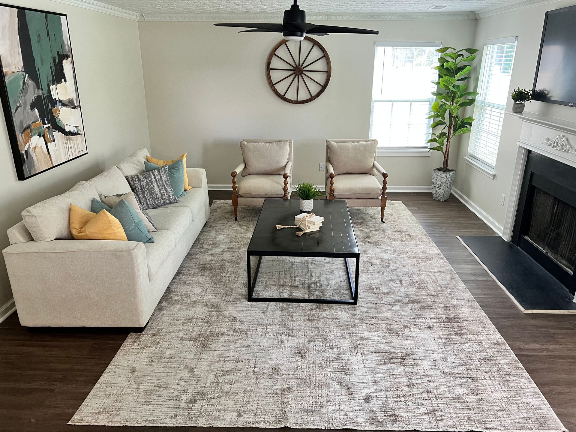 Living room with cream sofa, two armchairs, rug, coffee table, fireplace, artwork, and large decorative wheel.