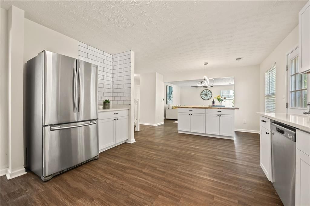 Spacious kitchen with stainless steel refrigerator, white cabinets, and wooden floors.