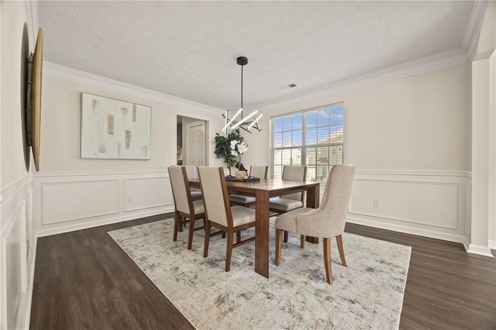 Dining room with wood table, six chairs, rug, artwork, and window.