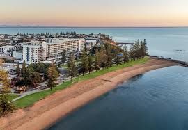 Aerial view of beachfront apartments beside a sandy shore and calm blue water at sunset