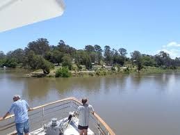 Two people on a boat looking over a calm river with trees along the far bank