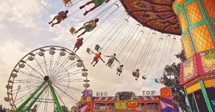Amusement park with spinning swing ride, Ferris wheel, and colorful booths under a cloudy sky
