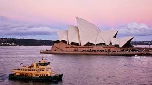 Sydney Opera House with a ferry on the water, pink and purple sky at dusk.
