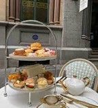 Tiered tray of treats for afternoon tea, with teapot and chair set outside.