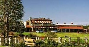 Two-story building with awnings, surrounded by grass and a fence, with cars parked out front, under a blue sky.