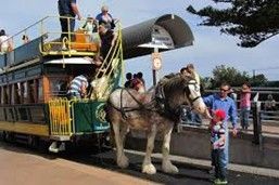 Horse-drawn tram with passengers. A person pets the horse, a child looks on.