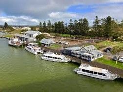 Boats docked near buildings on a green waterway. Cloudy sky overhead.