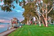 Two-story building with awnings, surrounded by grass and a fence, with cars parked out front, under a blue sky.