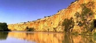 Park scene with red-roofed gazebo, green lawn, trees, and cloudy blue sky.