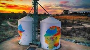 Two white silos painted with colorful murals against a sunset sky.