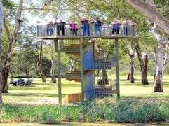 Observation tower with spiral staircase and people on top, surrounded by trees and a green landscape.