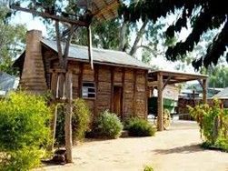 Wooden cabin with chimney, porch, and windmill; surrounded by greenery and wagon.