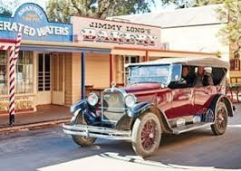 Vintage red car parked on a street in front of shops, resembling an old Western town.