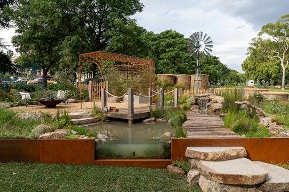 Rustic garden with pond, wooden bridge, waterfall, and windmill.