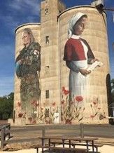 Mural on silos: soldier, medical worker in red jacket, holding letter, surrounded by poppies.