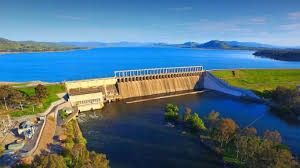 Dam on a large lake, with clear blue water and green grassy banks.
