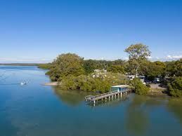 Calm blue bay with a small dock, trees, and a shoreline under clear sky