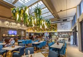 Bright modern restaurant interior with blue chairs, hanging plants, and skylit ceiling