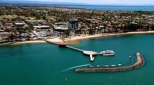 Aerial view of a turquoise harbor with a long pier and breakwater beside a coastal town
