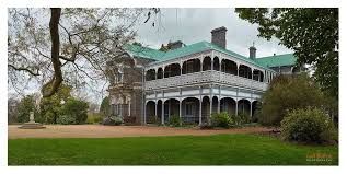 A large white house with a green roof is surrounded by trees and grass.