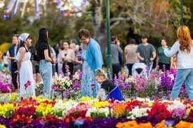 People in a colorful flower garden, some looking at flowers, others taking photos, a child is kneeling.