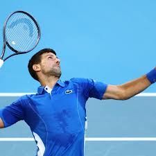 Novak Djokovic serving a tennis ball in blue attire.