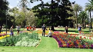 Park with flowerbeds, people, and trees on a sunny day.
