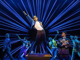 A performer on stage in front of a blue light display, with backup dancers.